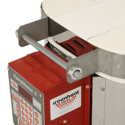 Close-up of a RampMaster II electric oven control panel mounted on a red Evenheat Enthusiast oven, with a metal support bracket and part of a white ceramic oven tray visible against a white background.